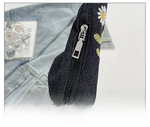 Détail d'une fermeture éclair fluide et broderie marguerite sur un sac bandoulière en jean