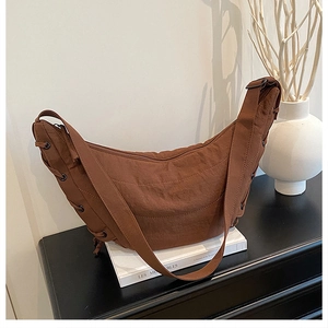 Detail of a brown crescent shoulder bag with lace-up side accents on a white book