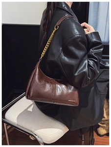 Detail of dark brown leather handbag with gold chain strap and brand logo on textured surface