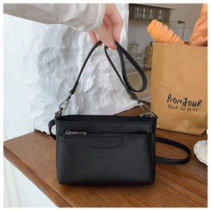 Detail of black pebbled PU leather crossbody bag with front zipper and silver hardware