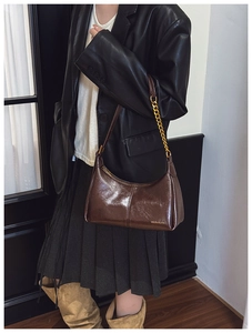 Detail view of dark brown patent leather hobo bag with gold chain and branded logo