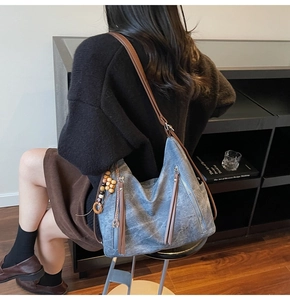 Detail view of washed gray-blue shoulder bag with leather straps and wood bead charm
