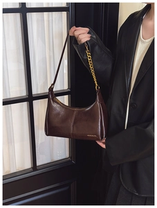 Detail of dark brown glossy leather crescent bag with gold chain and thin shoulder strap