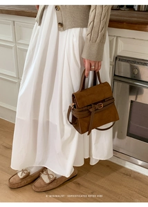 Bolso bandolera de ante marrón con detalle de hebilla retro en un ambiente minimalista