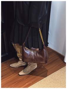Detailed close-up of dark brown glossy leather shoulder bag with gold chain strap detail