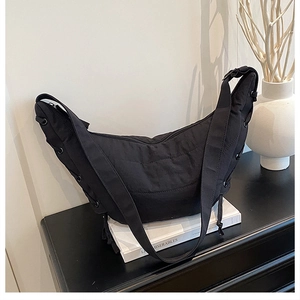 Detail of a black crescent crossbody bag with quilted texture and metal eyelet drawstrings