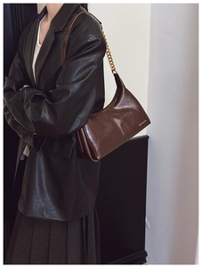 Detail of dark brown glossy leather texture with golden metal chain strap on hobo bag