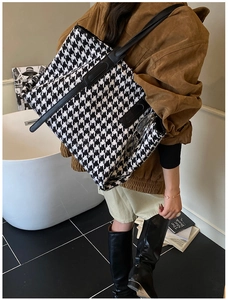 Classic houndstooth tote bag with black leather handles shown in a modern lifestyle setting