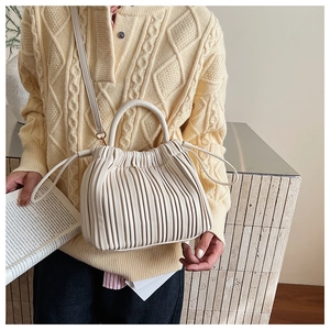 Detail of cream pleated bucket bag showing vertical folds and curved handle texture