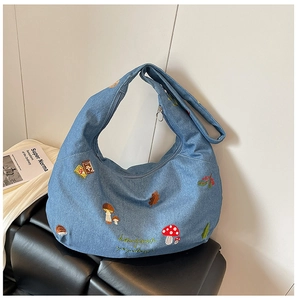 Détail du sac croissant en jean bleu clair avec broderies de champignons et hérisson