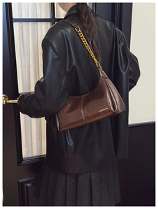 Deep brown glossy slouchy shoulder bag with gold chain strap on a stylish model