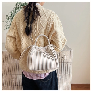 Detailed view of beige pleated bucket bag on a model wearing a cozy knitted sweater