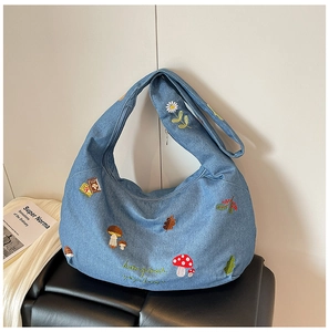 Détail du sac demi-lune en denim bleu clair avec broderies de fleurs et texte bonjour