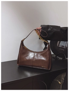 Close-up of deep brown glossy leather bag featuring gold chain and embossed logo