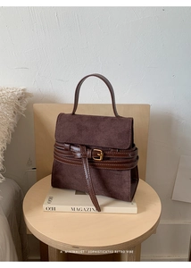 Detalle de bolso de ante marrón oscuro con ribetes de cuero y hebillas metálicas doradas