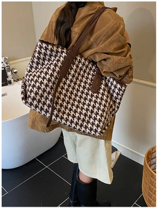 Detail of large houndstooth tote bag with brown leather handles worn by a model