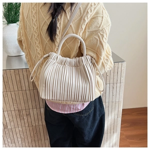 Close-up of pleated cream beige bucket bag with round handle and drawstring detail