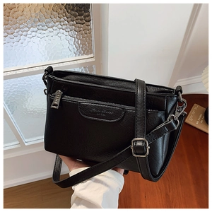 Detail of black pebbled PU leather crossbody bag featuring silver zippers and hardware