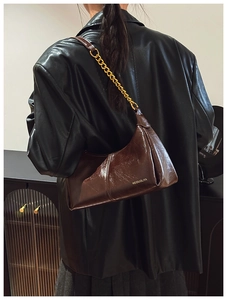 Close-up of brown glossy leather shoulder bag with a gold chain strap and branding