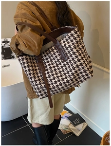 Detail view of large houndstooth tote bag with brown leather straps and metal hardware
