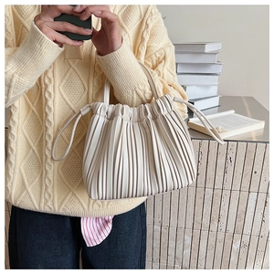 Detailed view of cream pleated bucket bag with synthetic leather texture and drawstring