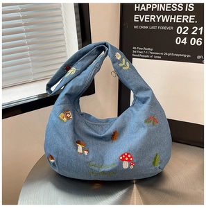 Détail d'un sac hobo en jean bleu avec des broderies complexes de champignons et fleurs