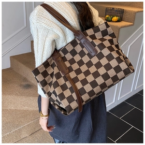 Detailed view of large checkered canvas tote bag with brown leather handles worn on shoulder
