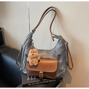 Dettaglio borsa tote in tela grigia con tasca in pelle marrone e ciondolo peluche