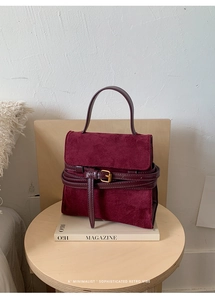 Primer plano de bolso vintage color burdeos con detalle de hebilla sobre una revista
