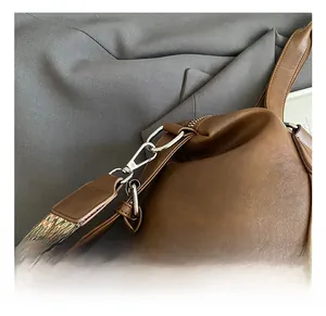 Detail of silver metal swivel hook and colorful geometric woven strap on brown leather bag