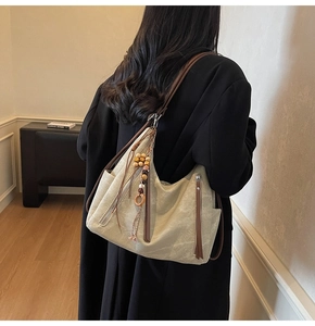 Detail of fabric hobo bag featuring side zip pockets and ethnic tassel with wooden beads