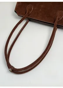 Close-up of brown suede tote bag featuring reinforced handle stitching and leather loop detail