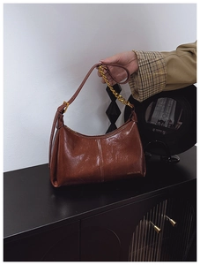 Detail of glossy brown leather hobo bag with a gold metal chain strap and logo