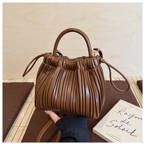 Detail of pleated brown leather bucket bag with rigid handle and drawstring closure