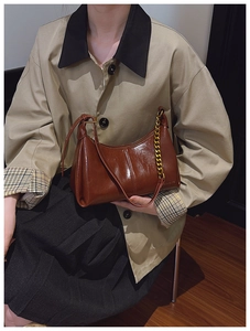 Detail of glossy brown hobo bag with adjustable leather strap and decorative gold chain