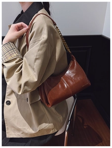 Detailed close-up of brown glossy PU leather bag with gold chain and brand logo