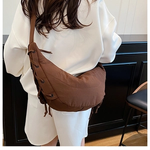 Detail of brown crescent bag with decorative side lacing and metal eyelets on wide strap