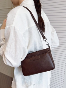 Brown leather crossbody square bag with embossed logo worn by model in minimalist setting
