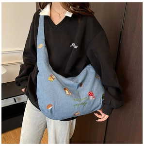 Détails de broderies champignons et hérissons sur un sac besace en jean bleu délavé