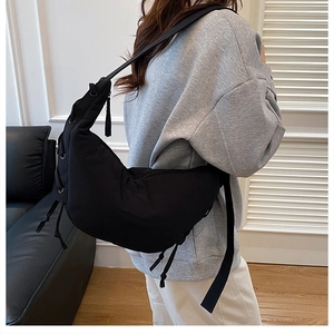 Detail of a black crescent crossbody bag showing drawstring ties and shoulder strap buckle
