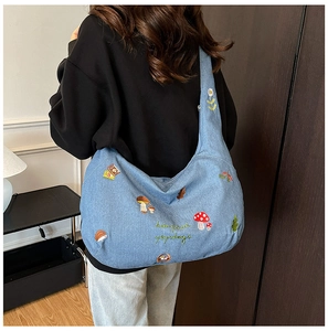 Détails de broderie de champignons et animaux sur un sac hobo en jean bleu sur modèle