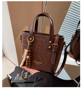 Detail view of brown retro bucket bag with gold rivets and ethnic bead charm accessory