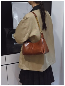 Close-up of caramel leather shoulder bag featuring gold chain strap and metal logo detail