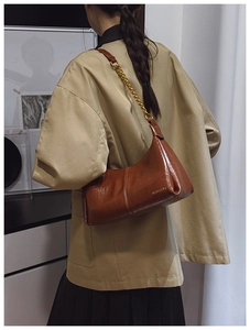 Detail of dark brown glossy leather shoulder bag featuring gold chain and brand logo