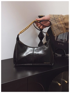 Detail of glossy black hobo bag featuring chunky gold chain and metallic brand logo