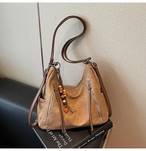 Detail of camel tote bag with double metal zippers, wooden beads, and fringe tassel