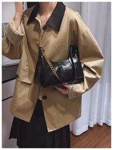Detail of black glossy faux leather bag with chunky gold chain and thin shoulder strap