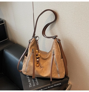 Detail of tan hobo bag featuring decorative leather tassels and functional side zippers