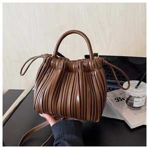 Close-up of pleated texture on a brown bucket bag with a laptop and coffee in the background