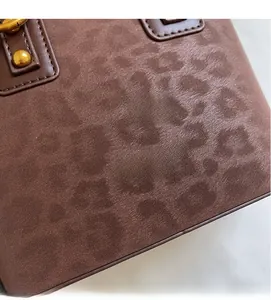 Detail of dark brown matte leather bag with leopard print and gold hardware